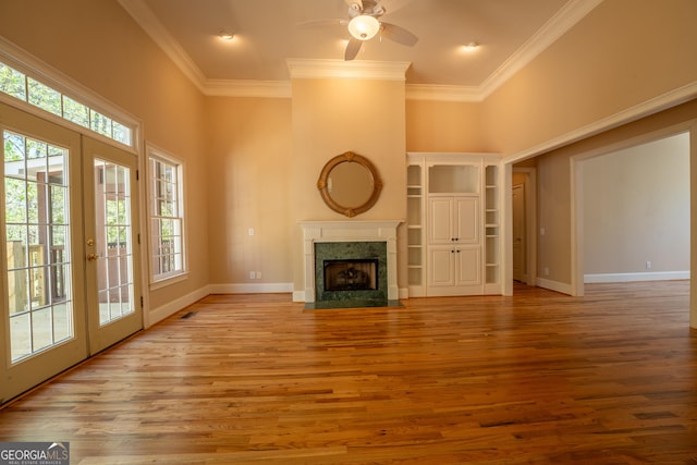 unfurnished living room with a premium fireplace, crown molding, a ceiling fan, and french doors