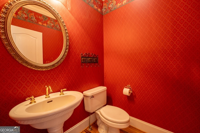 half bath featuring wood finished floors, toilet, baseboards, and a sink