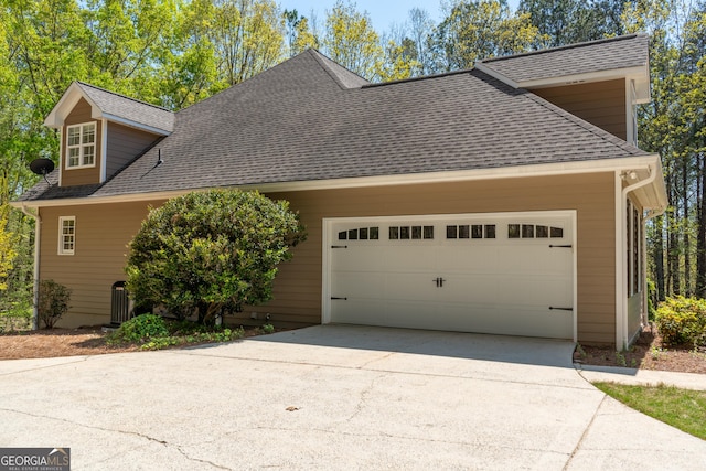 view of front of property featuring concrete driveway, cooling unit, a garage, and a shingled roof