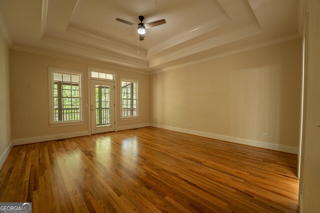 empty room featuring a tray ceiling, wood finished floors, baseboards, and ceiling fan