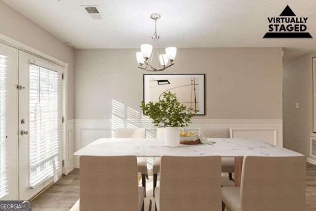 dining space with an inviting chandelier, french doors, visible vents, wainscoting, and light wood finished floors