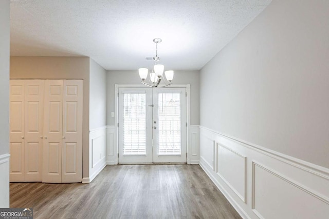 doorway to outside featuring wainscoting, a notable chandelier, wood finished floors, and a textured ceiling