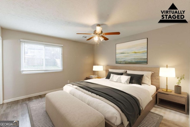 bedroom with a textured ceiling, light wood finished floors, baseboards, and a ceiling fan