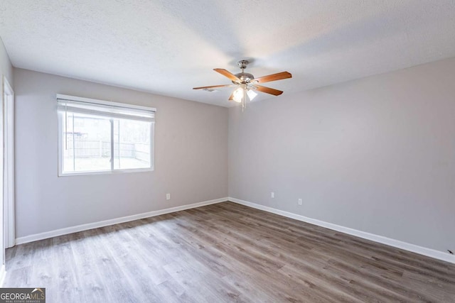 empty room featuring a textured ceiling, wood finished floors, baseboards, and a ceiling fan