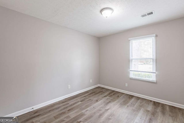 unfurnished room with visible vents, baseboards, a textured ceiling, and wood finished floors