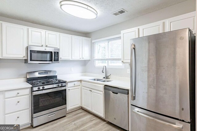 kitchen featuring visible vents, white cabinets, a sink, light wood finished floors, and stainless steel appliances