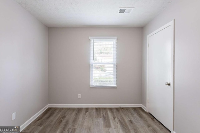 empty room featuring baseboards, visible vents, light wood-type flooring, and a textured ceiling