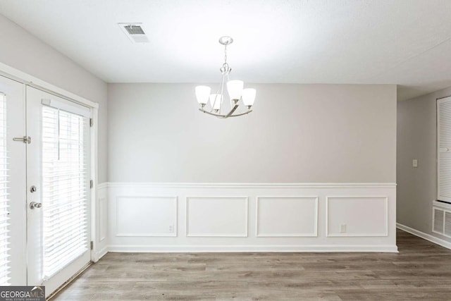 unfurnished dining area featuring wood finished floors, an inviting chandelier, wainscoting, and visible vents