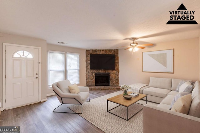 living room featuring a stone fireplace, visible vents, ceiling fan, and wood finished floors