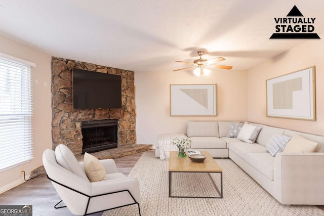 living room with a stone fireplace, a ceiling fan, and wood finished floors
