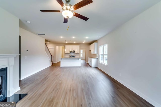 497 Principal Meridian Dr, Dallas, GA 30132 - unfurnished living room with wood finished floors, a fireplace with raised hearth, a ceiling fan, stairs, and recessed lighting