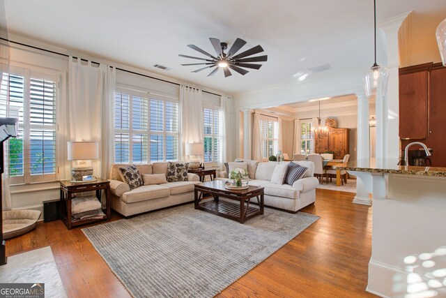 living area with a wealth of natural light, visible vents, wood finished floors, and ornamental molding