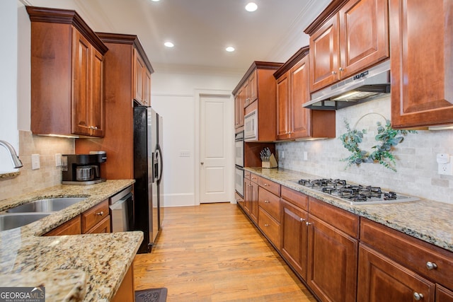 kitchen featuring light stone counters, a sink, light wood finished floors, appliances with stainless steel finishes, and under cabinet range hood
