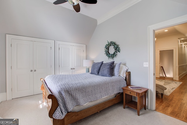 bedroom featuring lofted ceiling, light colored carpet, ornamental molding, multiple closets, and ceiling fan