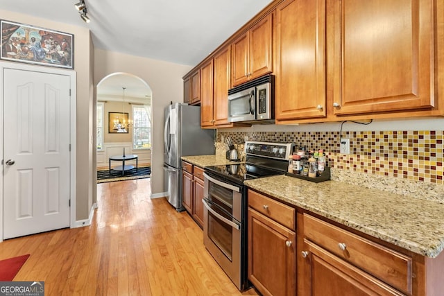 79 Tiffany Trce, Palmetto, GA 30268 - kitchen featuring light stone counters, appliances with stainless steel finishes, brown cabinetry, light wood-style flooring, and arched walkways