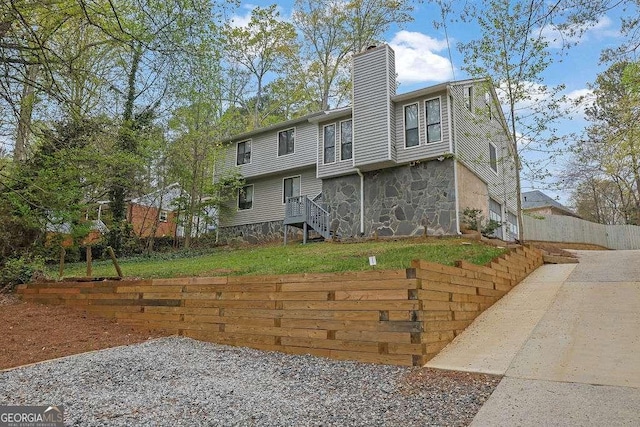rear view of property with a lawn, stone siding, a chimney, and fence