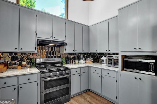 kitchen with backsplash, under cabinet range hood, stainless steel appliances, and light wood-type flooring