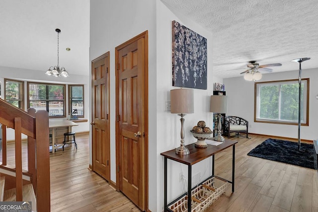 hall featuring light wood finished floors, an inviting chandelier, baseboards, and a textured ceiling