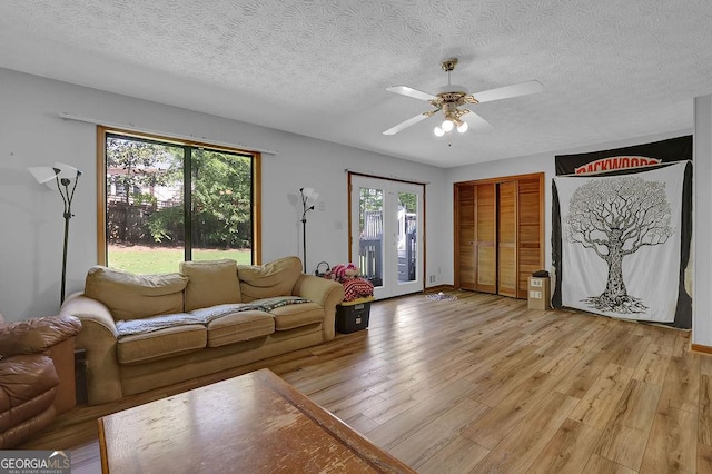 living area with ceiling fan, baseboards, light wood-style floors, and a textured ceiling