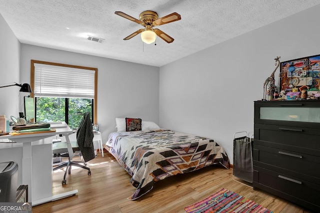 bedroom with light wood-style flooring, visible vents, a textured ceiling, and ceiling fan