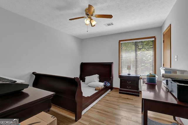 bedroom with light wood finished floors, visible vents, a textured ceiling, and ceiling fan