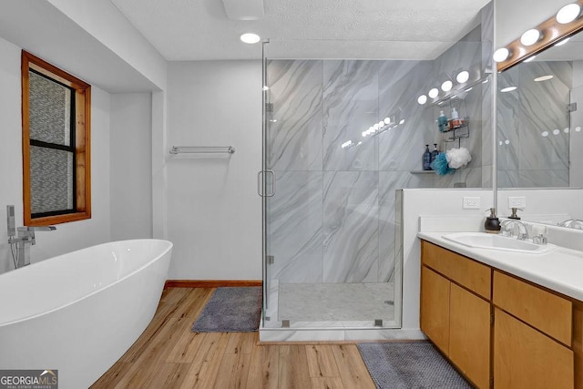 full bathroom with wood finished floors, a marble finish shower, a textured ceiling, vanity, and a soaking tub