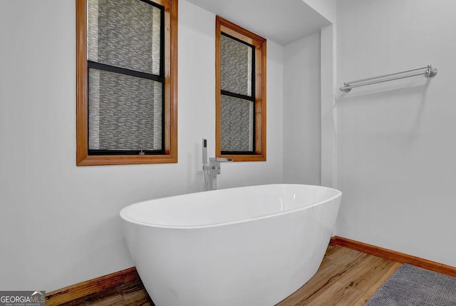 full bathroom with baseboards, wood finished floors, and a freestanding bath