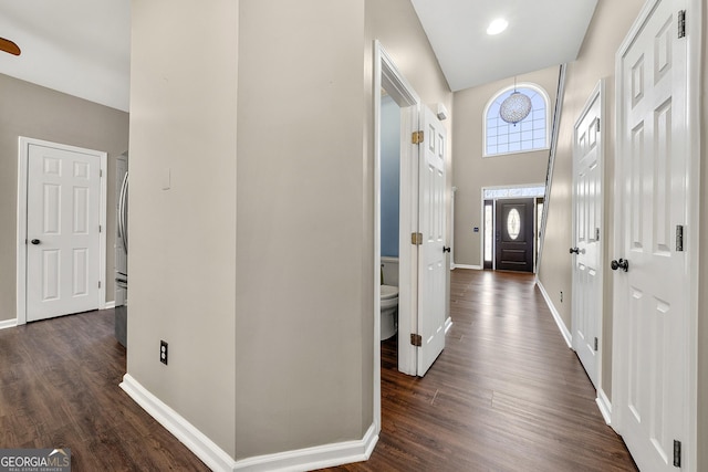 hallway featuring a high ceiling, dark wood-style floors, and baseboards