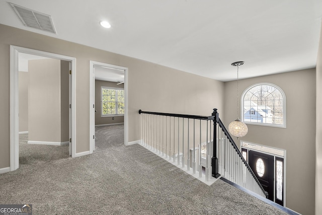 corridor with baseboards, an upstairs landing, visible vents, and carpet