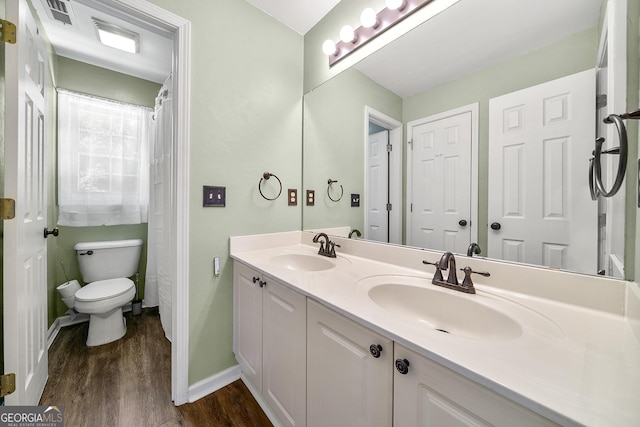 bathroom featuring toilet, wood finished floors, double vanity, and a sink