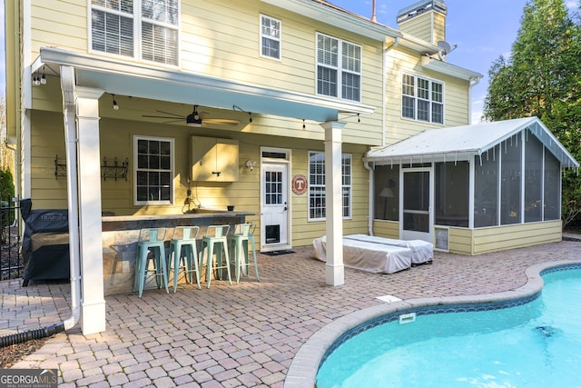 rear view of property with a chimney, outdoor dry bar, a sunroom, and a patio area