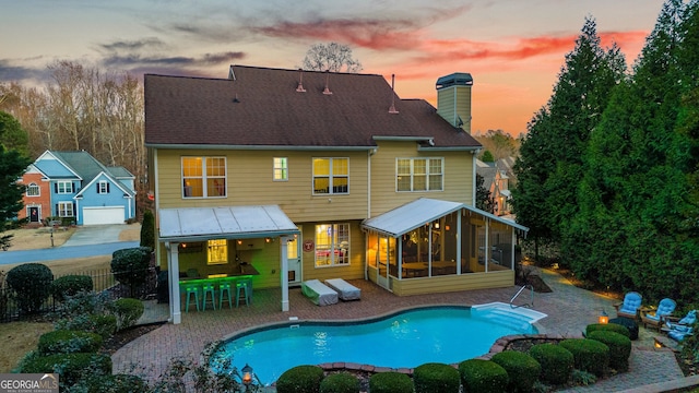 back of property at dusk with a sunroom, fence, a chimney, a fenced in pool, and a patio area