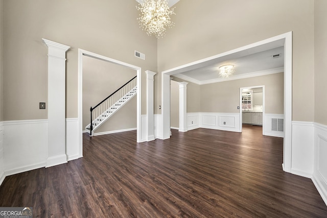 unfurnished living room featuring ornate columns, visible vents, a notable chandelier, and dark wood finished floors