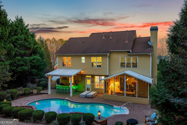 rear view of property with an outdoor pool, a patio, a shingled roof, and a chimney