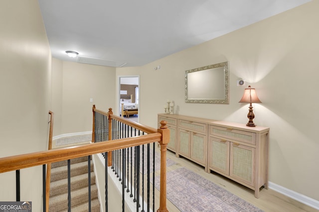corridor with an upstairs landing, light wood-style flooring, baseboards, and attic access