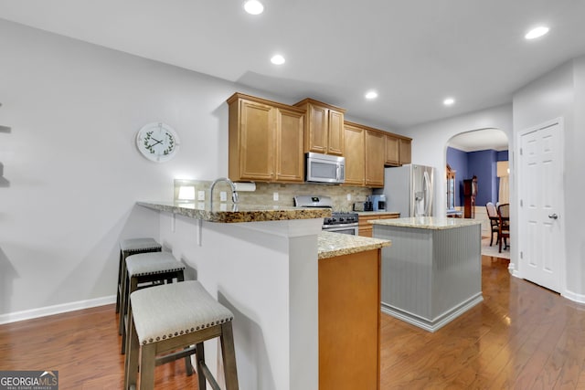 kitchen featuring a kitchen breakfast bar, dark wood-type flooring, arched walkways, stainless steel appliances, and decorative backsplash