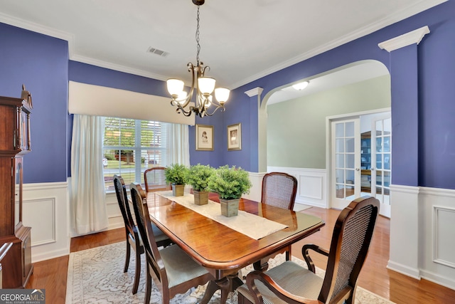 dining space featuring a chandelier, wainscoting, visible vents, arched walkways, and wood finished floors