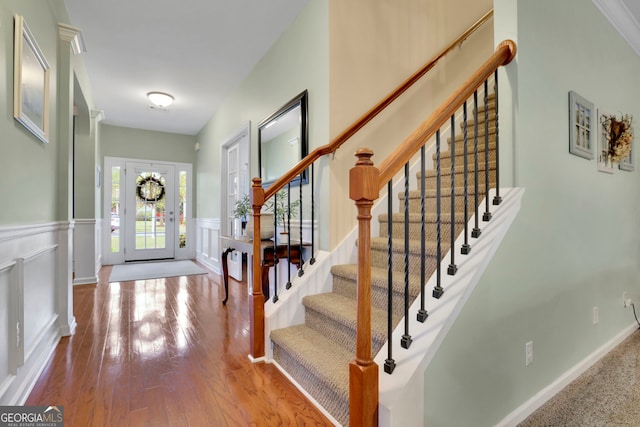 foyer with a decorative wall, stairway, wainscoting, and wood finished floors