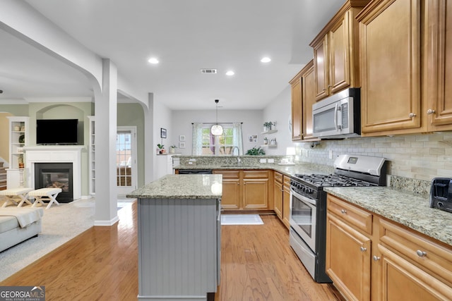 kitchen featuring open floor plan, a peninsula, light wood-type flooring, and stainless steel appliances