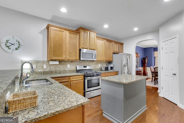 kitchen featuring arched walkways, appliances with stainless steel finishes, light wood finished floors, and a sink
