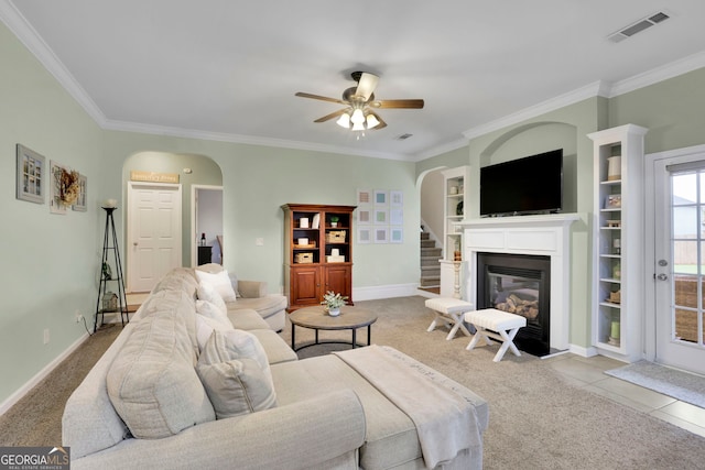 carpeted living area featuring visible vents, arched walkways, a ceiling fan, stairway, and a glass covered fireplace