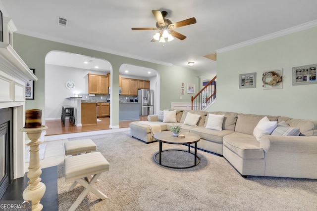 living area with visible vents, arched walkways, ceiling fan, crown molding, and stairs