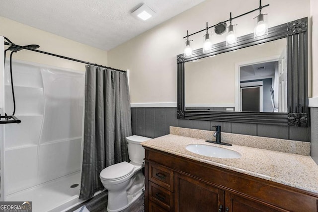 full bath with toilet, a textured ceiling, a shower stall, vanity, and wainscoting