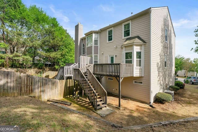 rear view of house with stairs, a wooden deck, fence, and a chimney