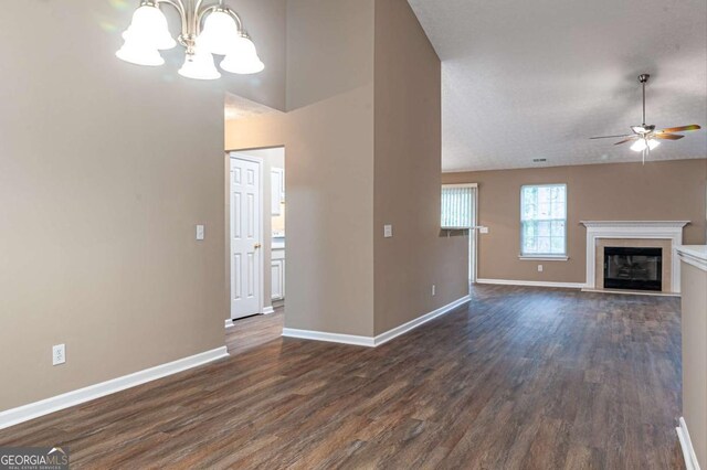 unfurnished living room with dark wood-style floors, ceiling fan with notable chandelier, baseboards, and a glass covered fireplace