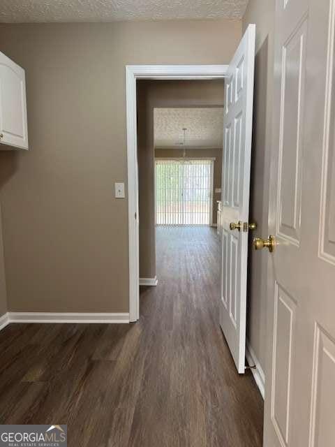hallway featuring baseboards, dark wood-type flooring, and a textured ceiling