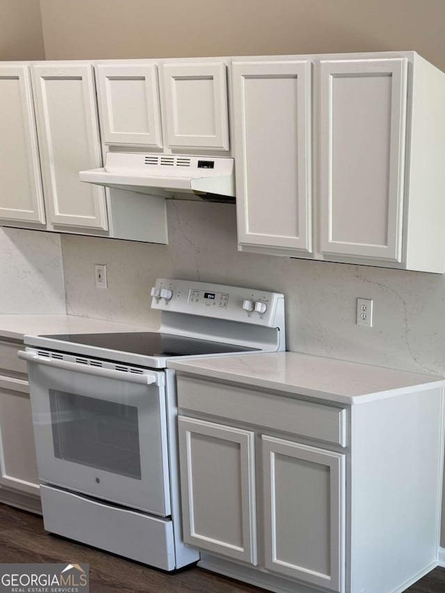 kitchen with under cabinet range hood, electric stove, light countertops, and dark wood finished floors