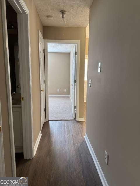 hall with dark wood-style flooring, baseboards, and a textured ceiling