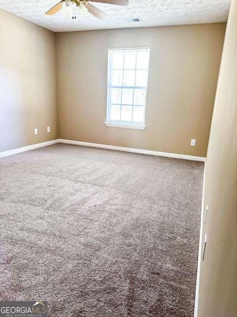 carpeted empty room with visible vents, a textured ceiling, baseboards, and ceiling fan