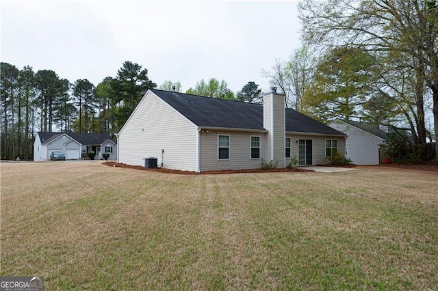 rear view of house with central AC unit, a chimney, and a yard